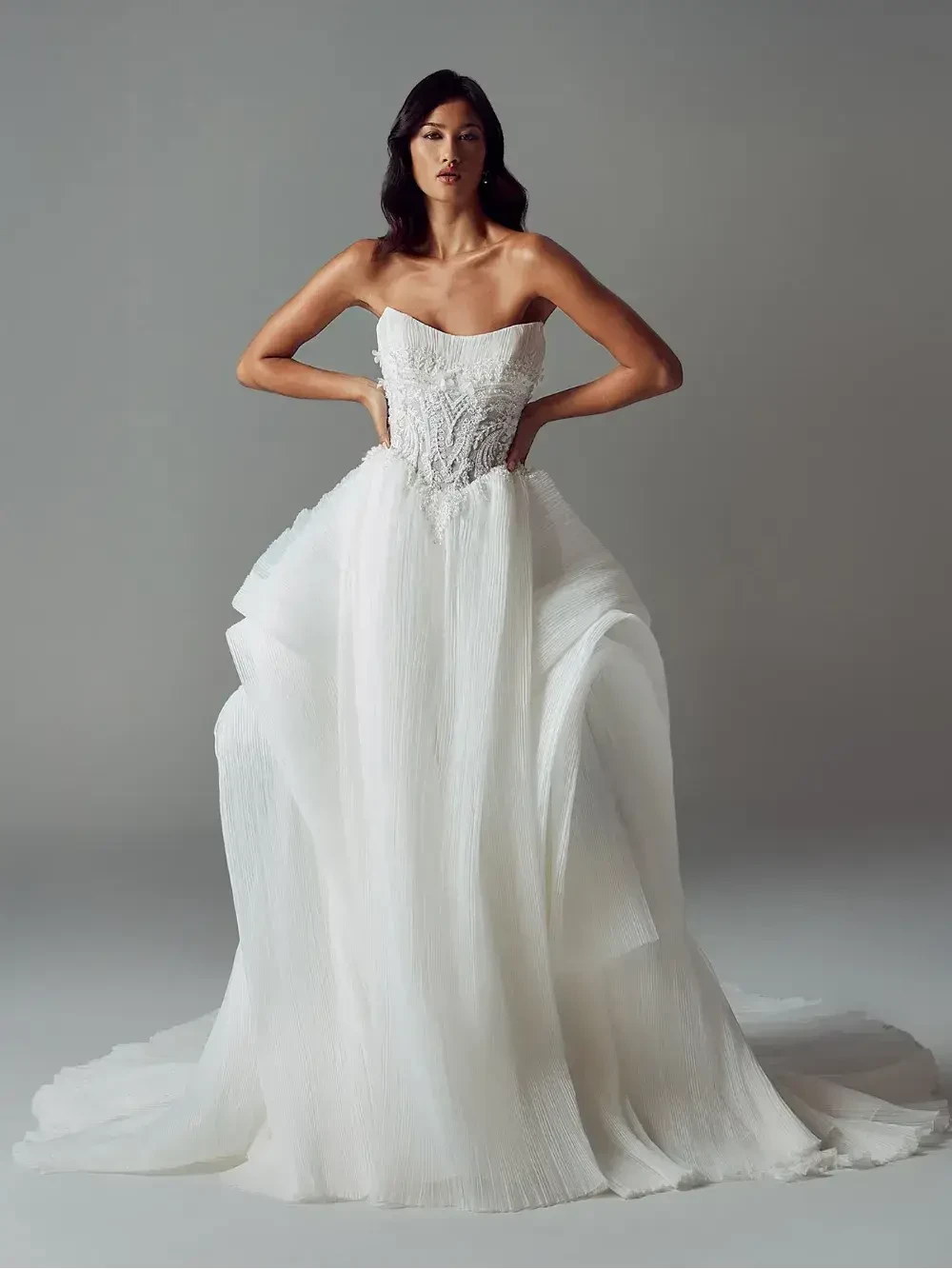 A model wearing an elegant white strapless wedding dress with a fitted bodice and flowing skirt, set against a neutral background.