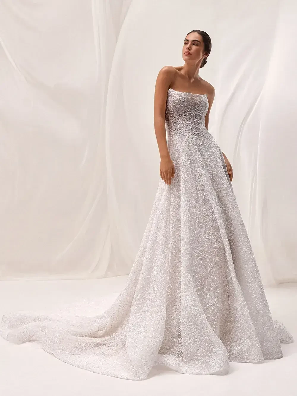 A model wearing a strapless, elegant white gown standing against a soft, neutral background.