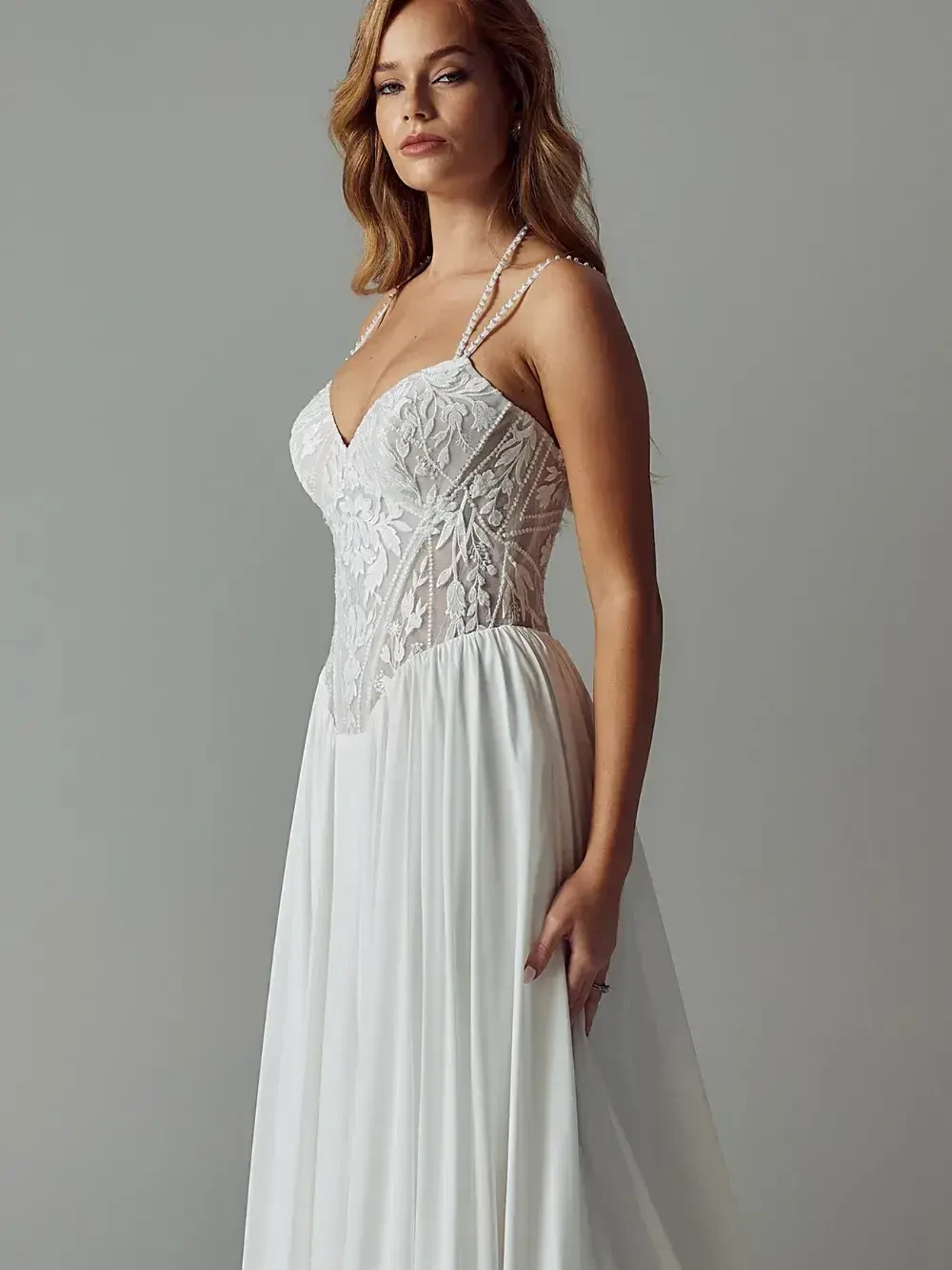 A woman wearing a white dress with intricate lace details on the bodice and a flowing skirt.