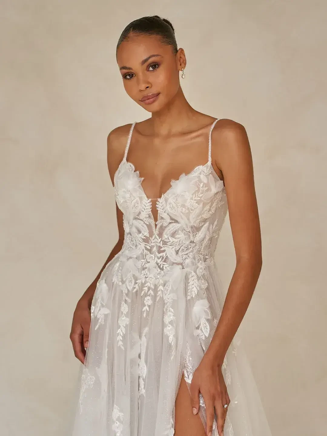 A woman modeling a delicate, lace wedding dress with floral details and a thigh-high slit.