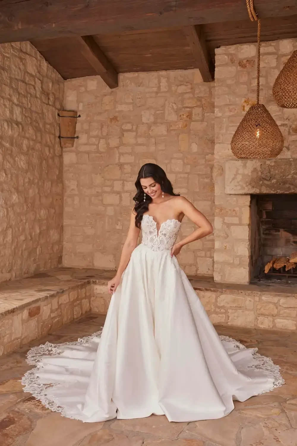 A woman in a strapless wedding dress standing in a stone room with a fireplace, showcasing a fitted bodice and a flowing skirt.